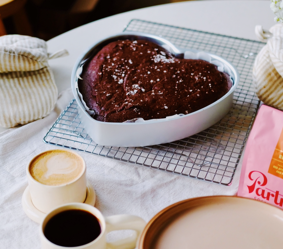 Heart-shaped dark chocolate espresso brownies cooling in a pan beside cups of coffee and a Partners Coffee bag