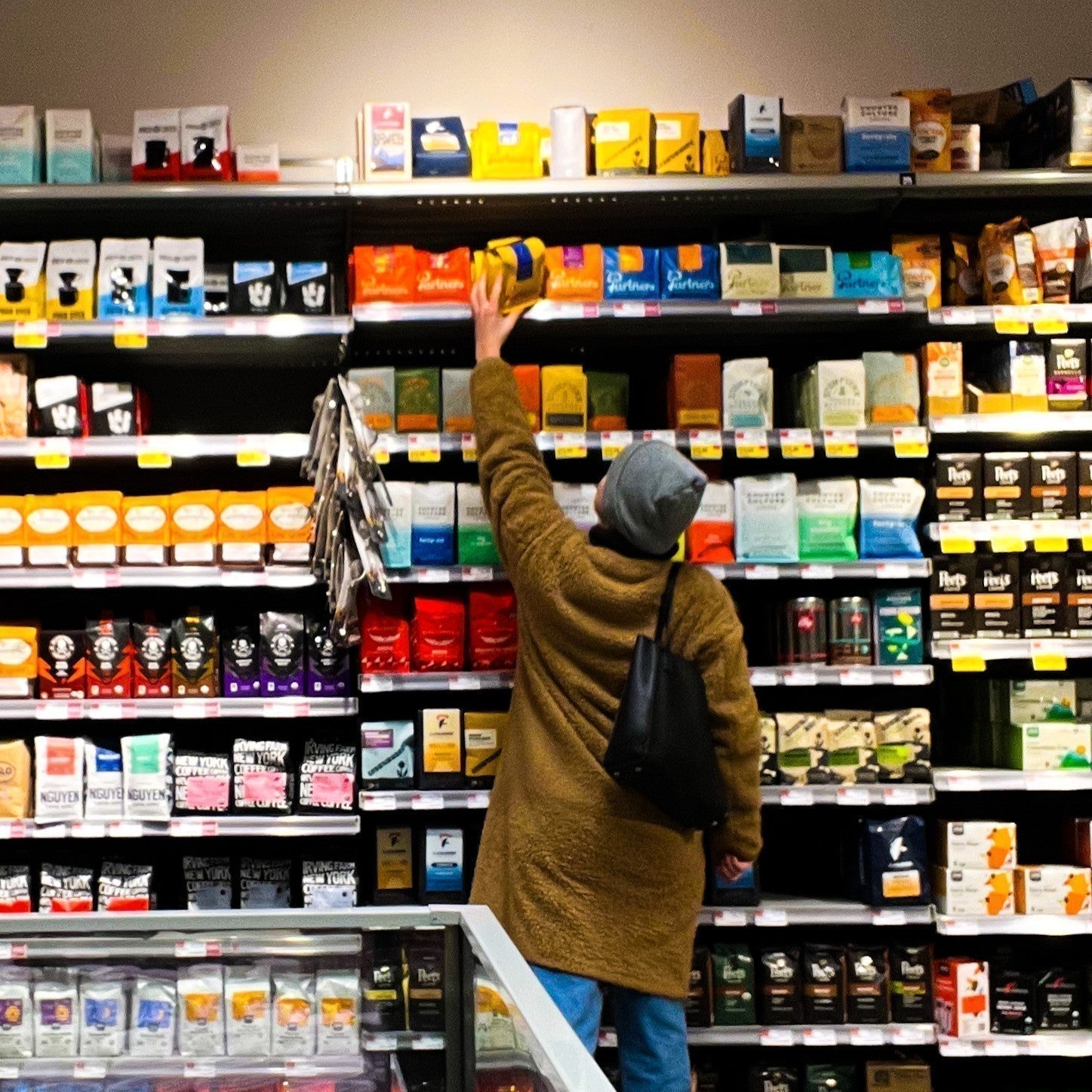Customer reaching for a yellow bag of Partners Coffee on a grocery store shelf