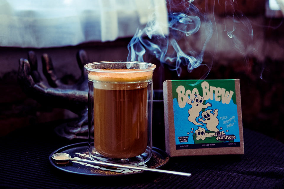 Front view of Boo Brew instant coffee package beside steaming coffee on a dark Halloween background