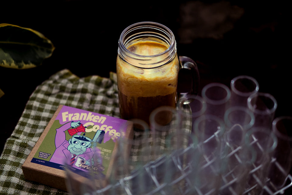 Franken Coffee specialty instant coffee beside a foamy iced coffee in a spooky Halloween setting