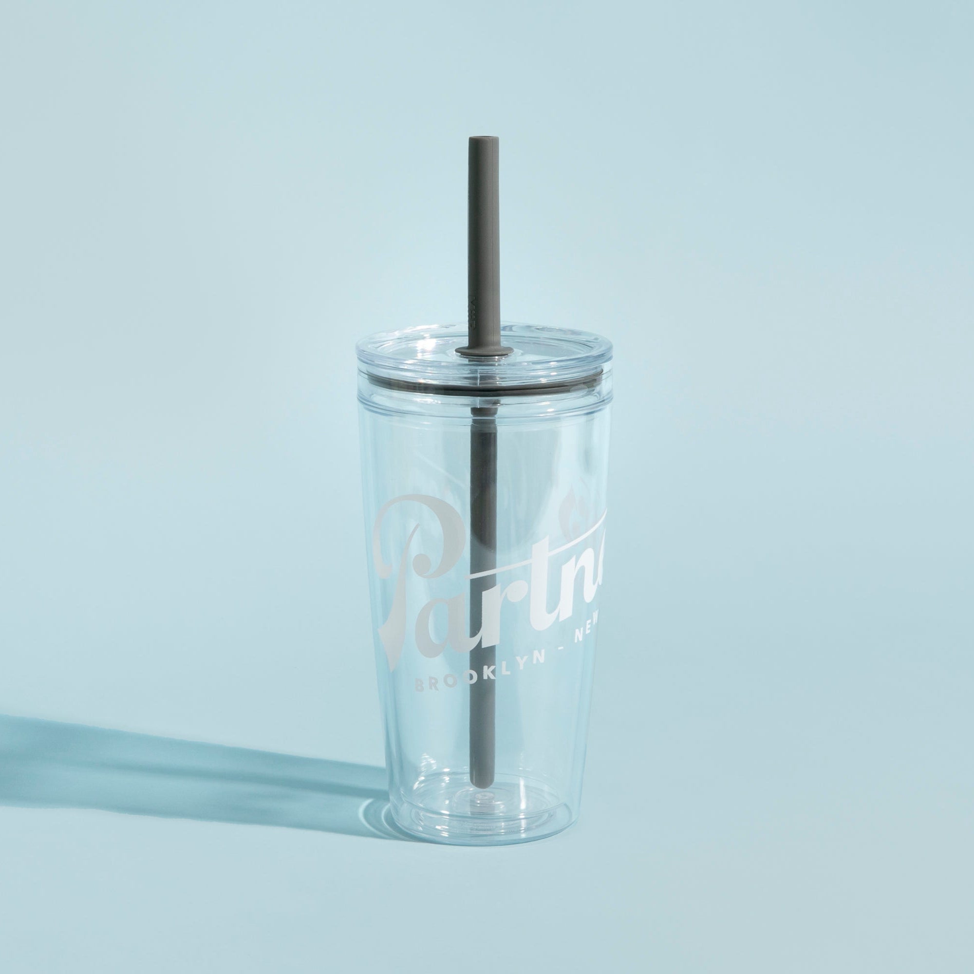 Front view of clear MiiR Everywhere Straw Tumbler showing double-wall body, black silicone straw and Partners logo on light blue background
