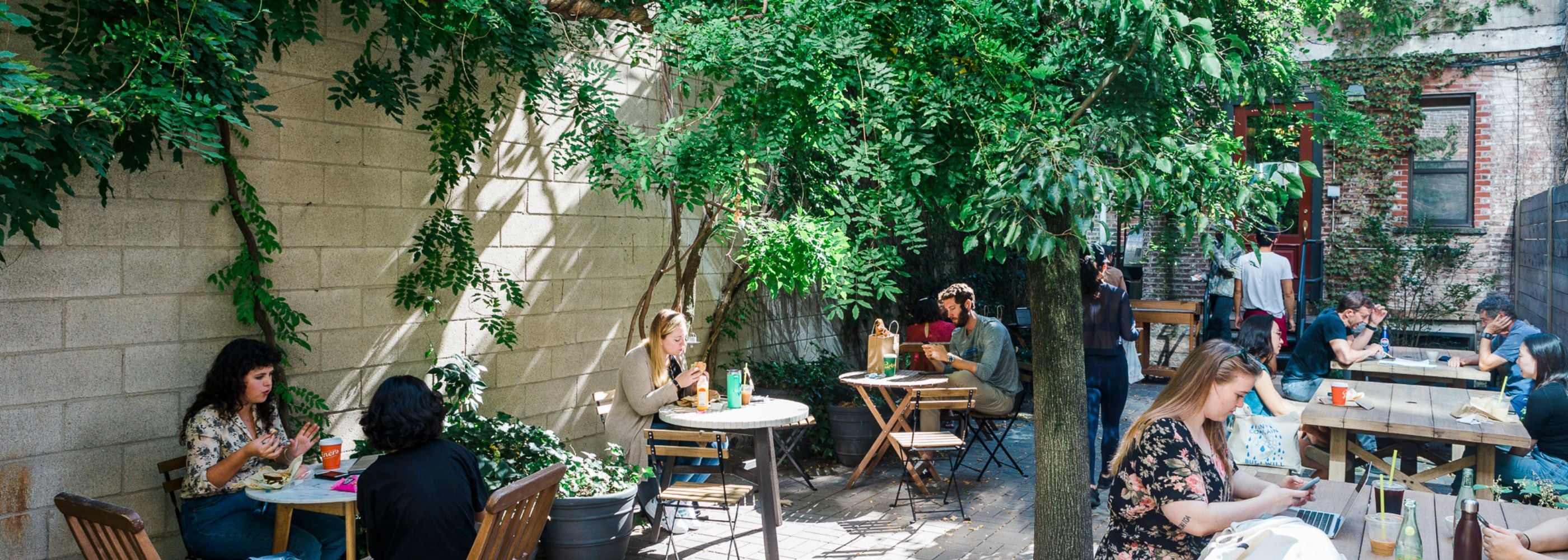 People sitting and drinking coffee at Partners Coffee’s tree-shaded outdoor patio in Long Island City
