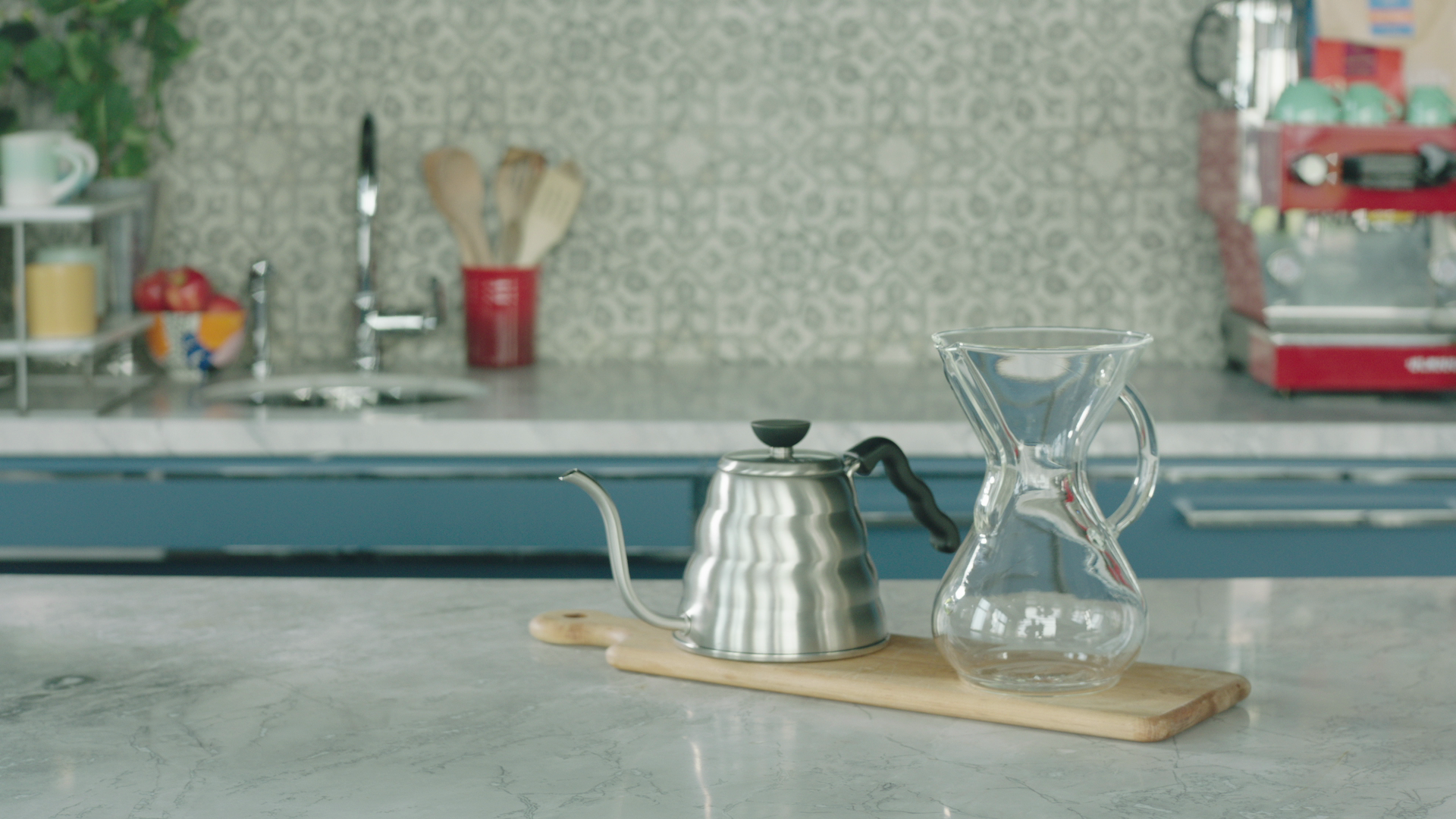 Front view of Chemex glass carafe showcasing its hourglass shape with a gooseneck kettle on a marble kitchen counter