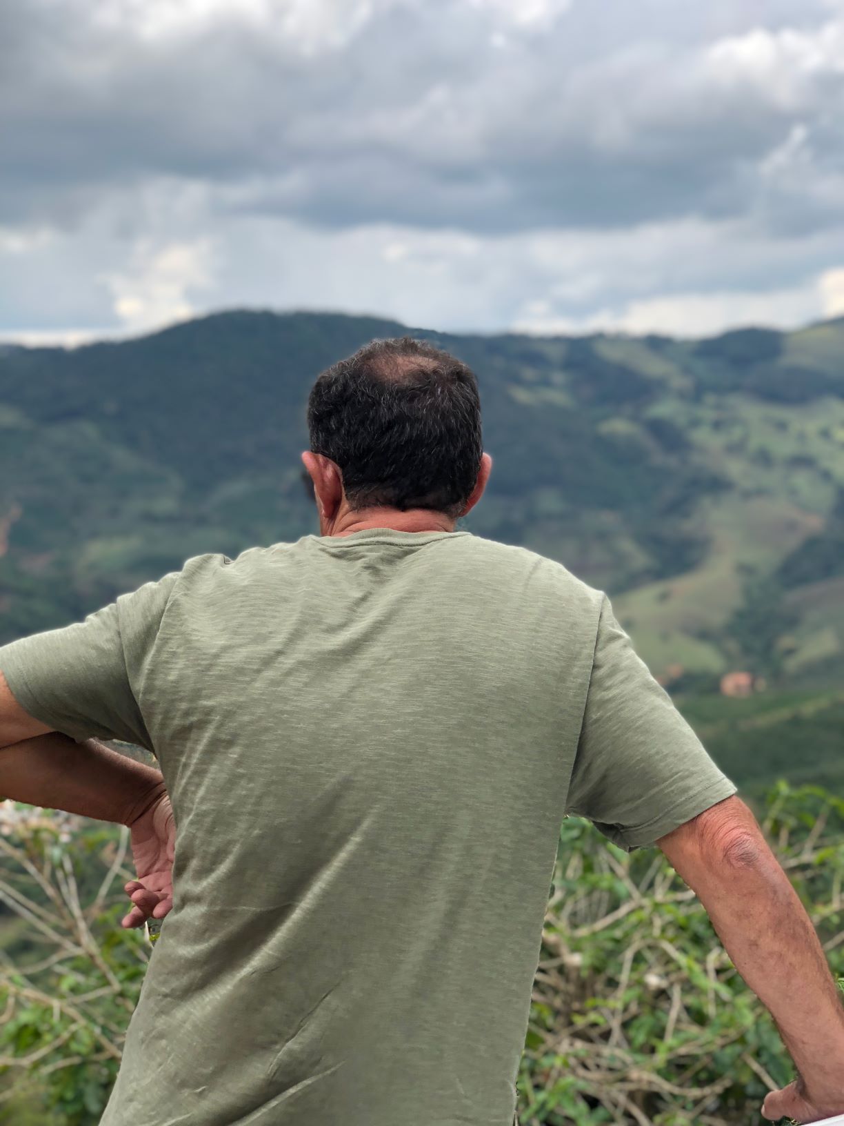 Man seen from behind standing with hands on hips, overlooking green hills near Furnas, Brazil