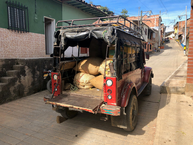 Red open-back truck carrying burlap sacks of green coffee parked on a narrow town street