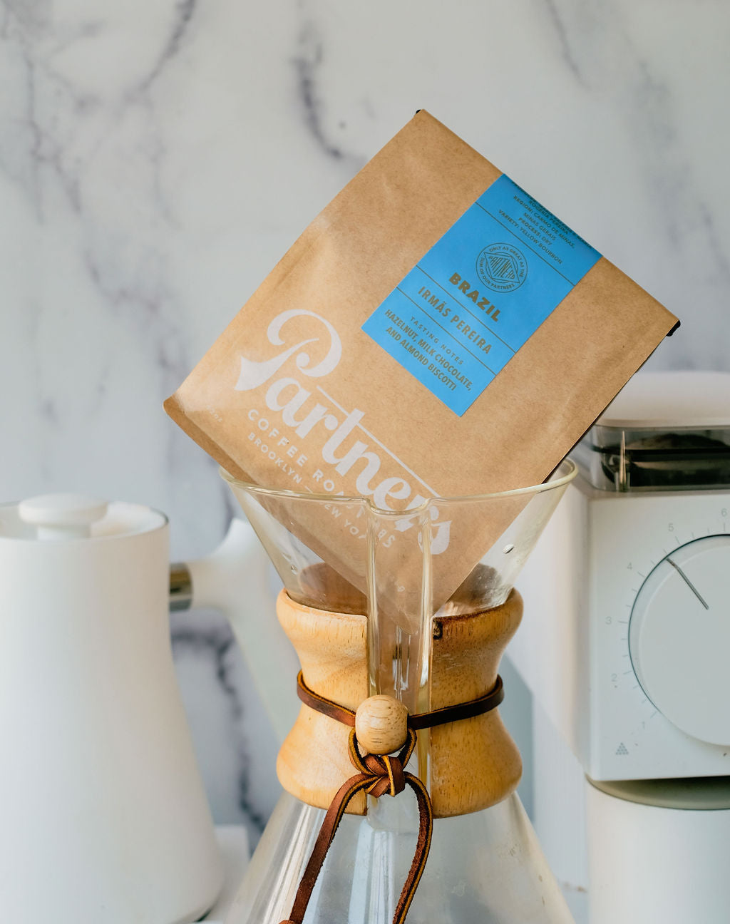 Angled view of a Brazil Irmãs Pereira kraft bag with blue label in a Chemex on a marble countertop
