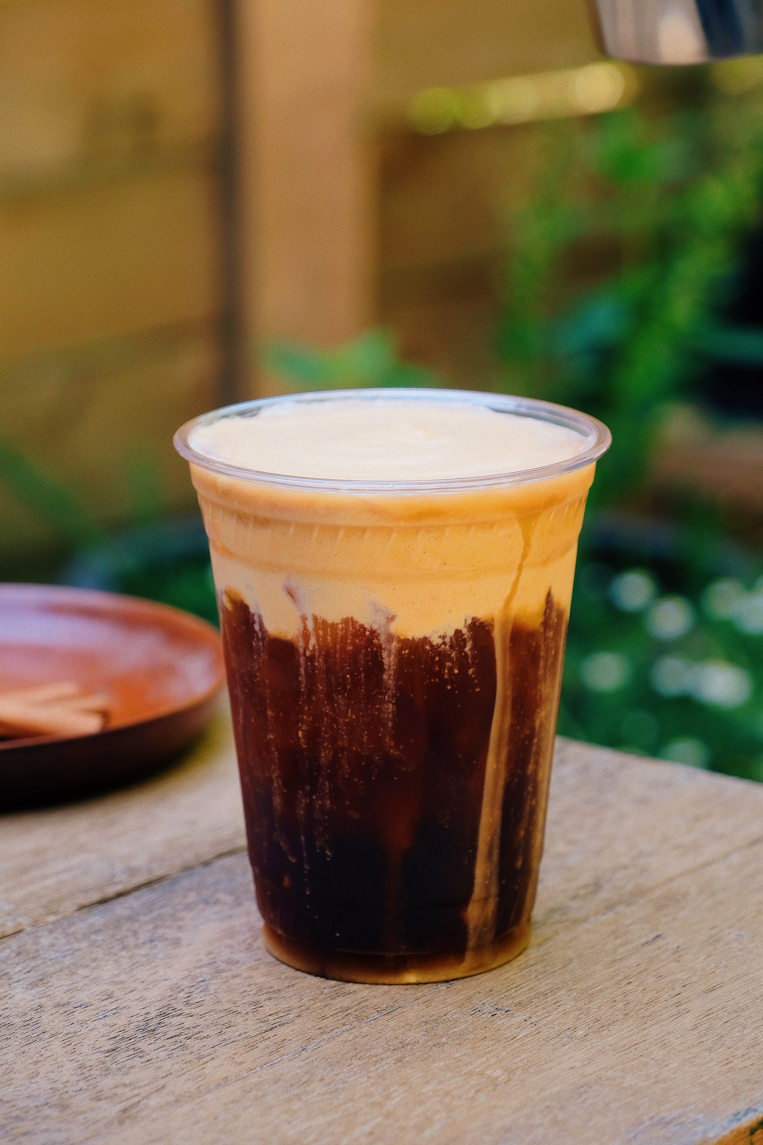 Close-up of iced cold brew topped with pumpkin cold foam, layered in a clear plastic cup on a wooden table