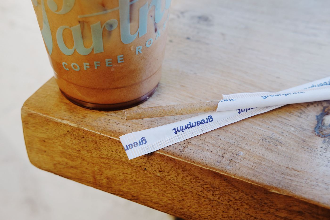 Close-up of an unwrapped agave straw next to a Partners Coffee iced cup showcasing the straw’s fibrous texture on a wooden table