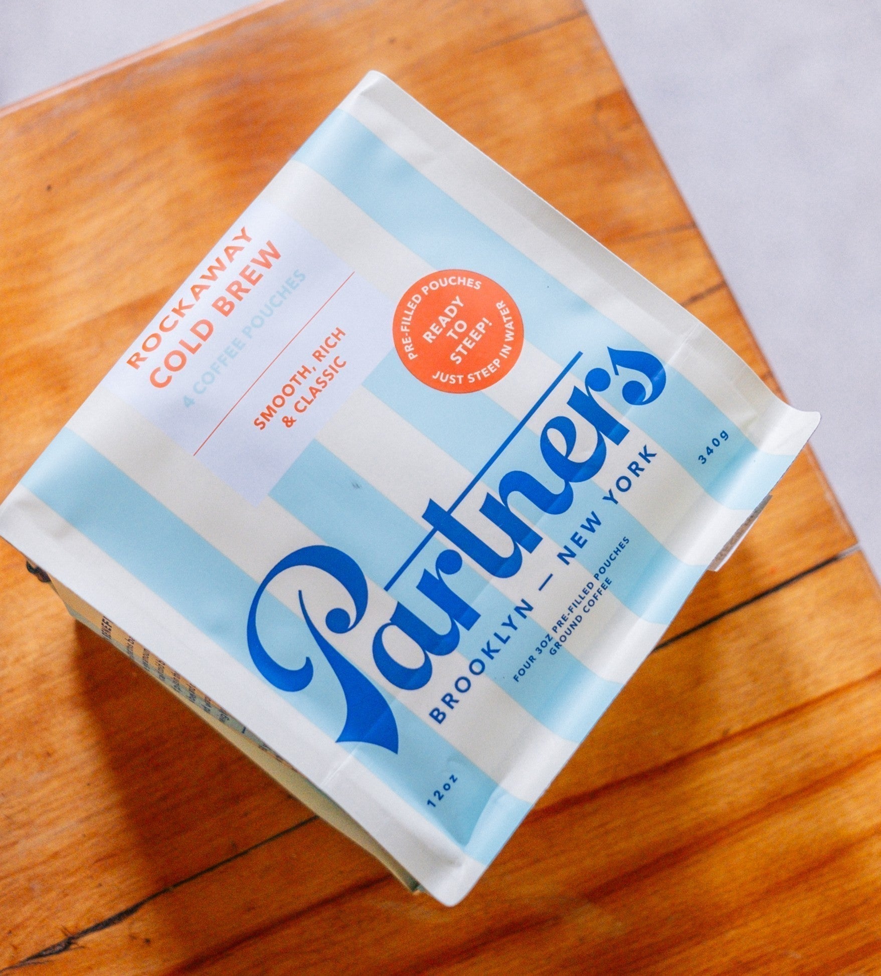 Angled top view of Rockaway Cold Brew pouch showing Partners Coffee blue-and-white striped bag with ‘Ready to Steep’ badge on a wooden board