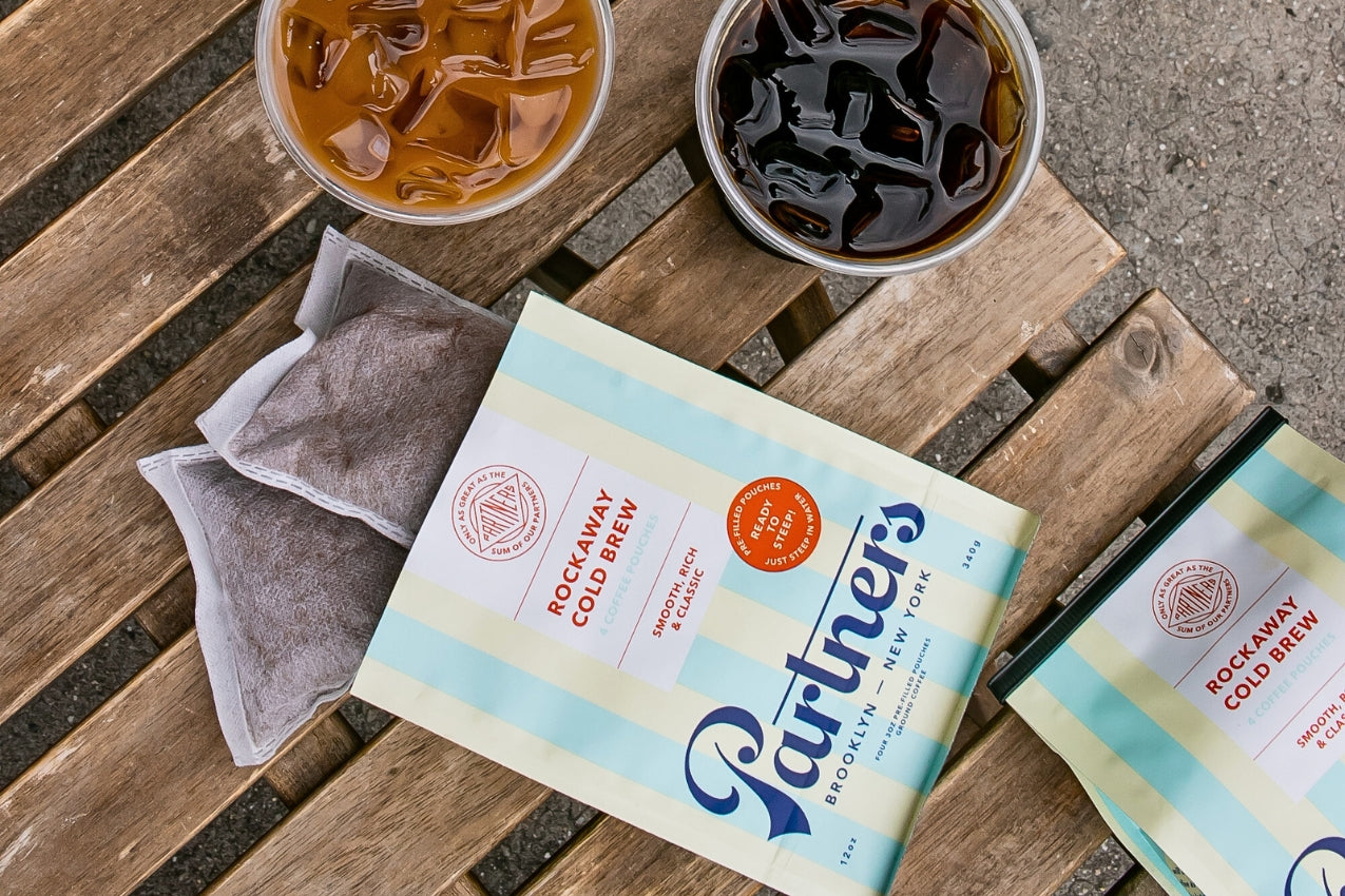 Overhead view of Rockaway Cold Brew pouch with two used brew pouches and two glasses of iced coffee on a wooden table