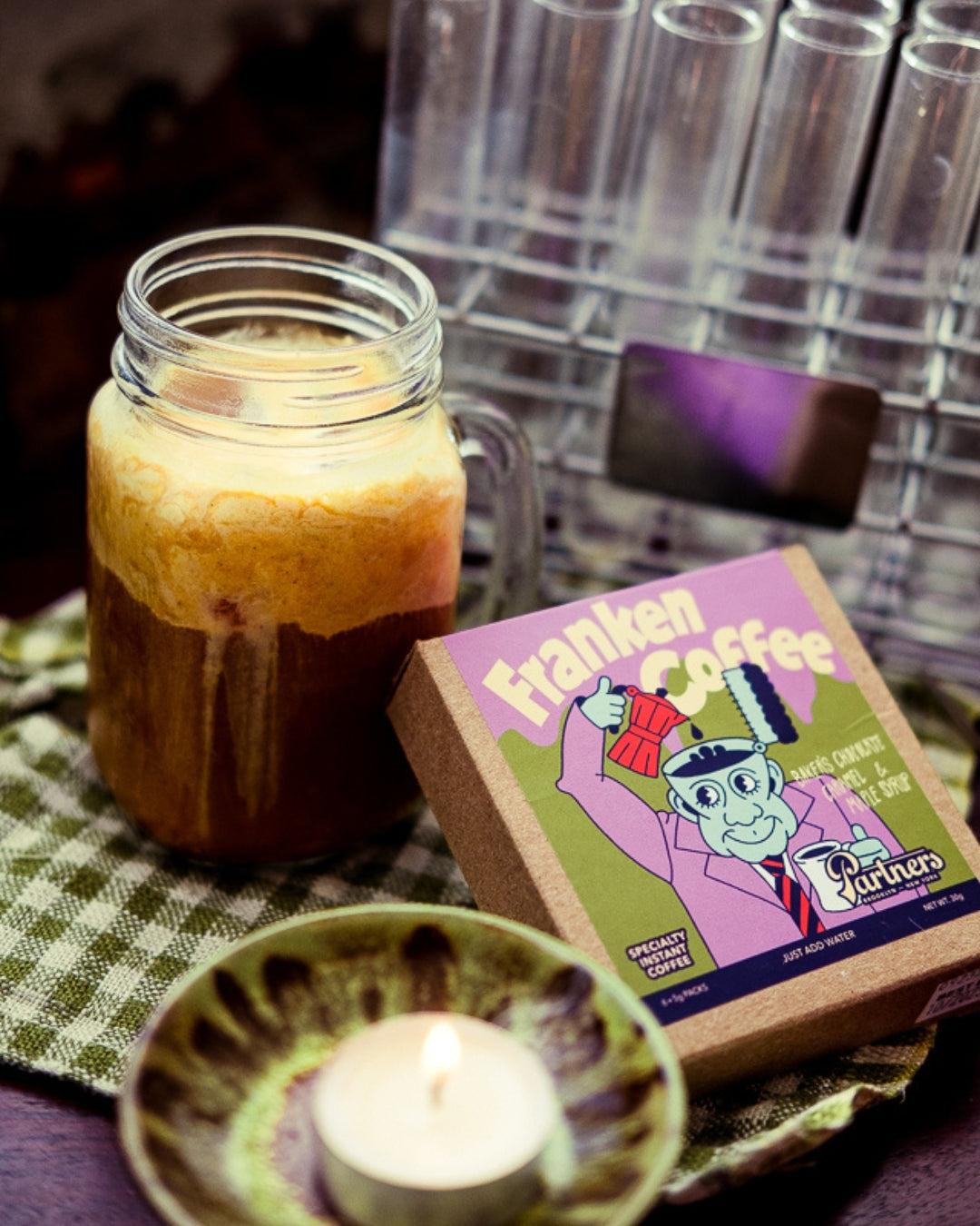 Three-quarter view of Franken Coffee instant coffee box beside a mason jar of frothy coffee with test tubes behind