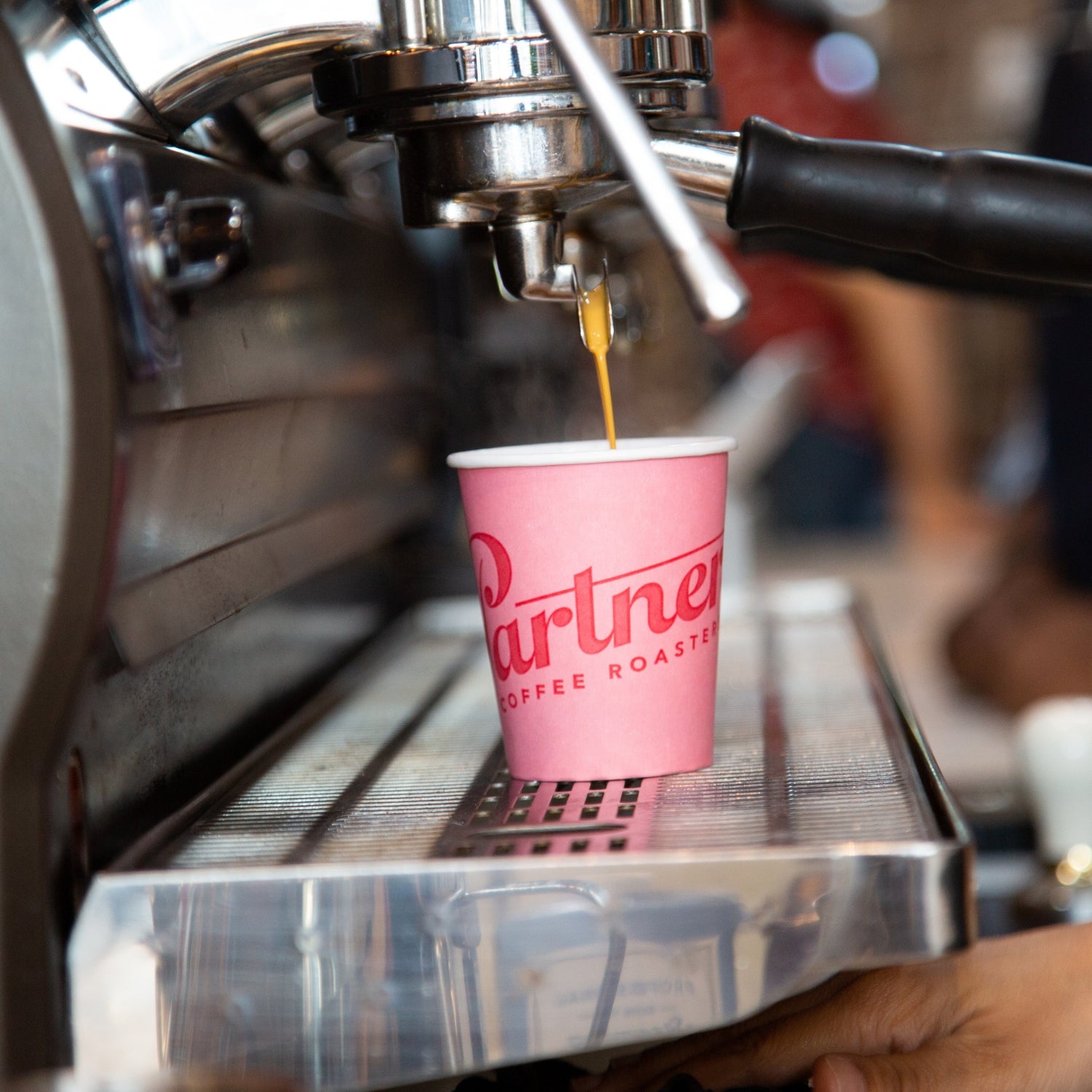 Barista pulling espresso into a pink paper cup labeled Partners Coffee Roasters on a stainless steel drip tray