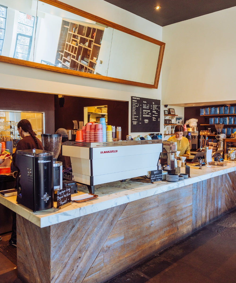 Baristas preparing coffee behind a marble counter at Partners Coffee Williamsburg with La Marzocco espresso machine