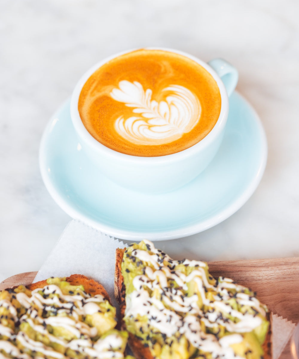 Latte with rosette latte art beside sesame avocado toast on a marble cafe table