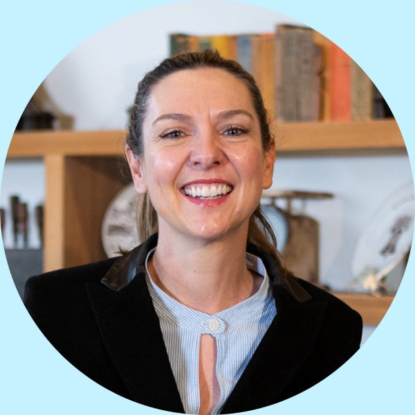 Smiling female team member wearing a black blazer, shoulder-up portrait in an office with wooden shelves and books