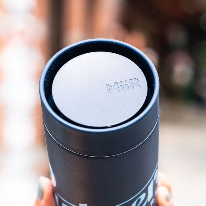 Top-down view of Partners x MiiR 360 Traveler travel mug showcasing its 360-degree drinking lid stamped with MiiR logo and blurred outdoor background