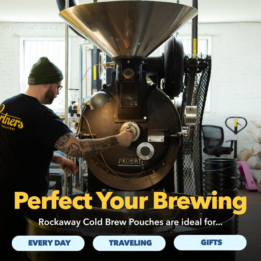 Man operating a Probat coffee roaster in a bright workshop, overlaid headline “Perfect Your Brewing” promoting Rockaway Cold Brew Pouches