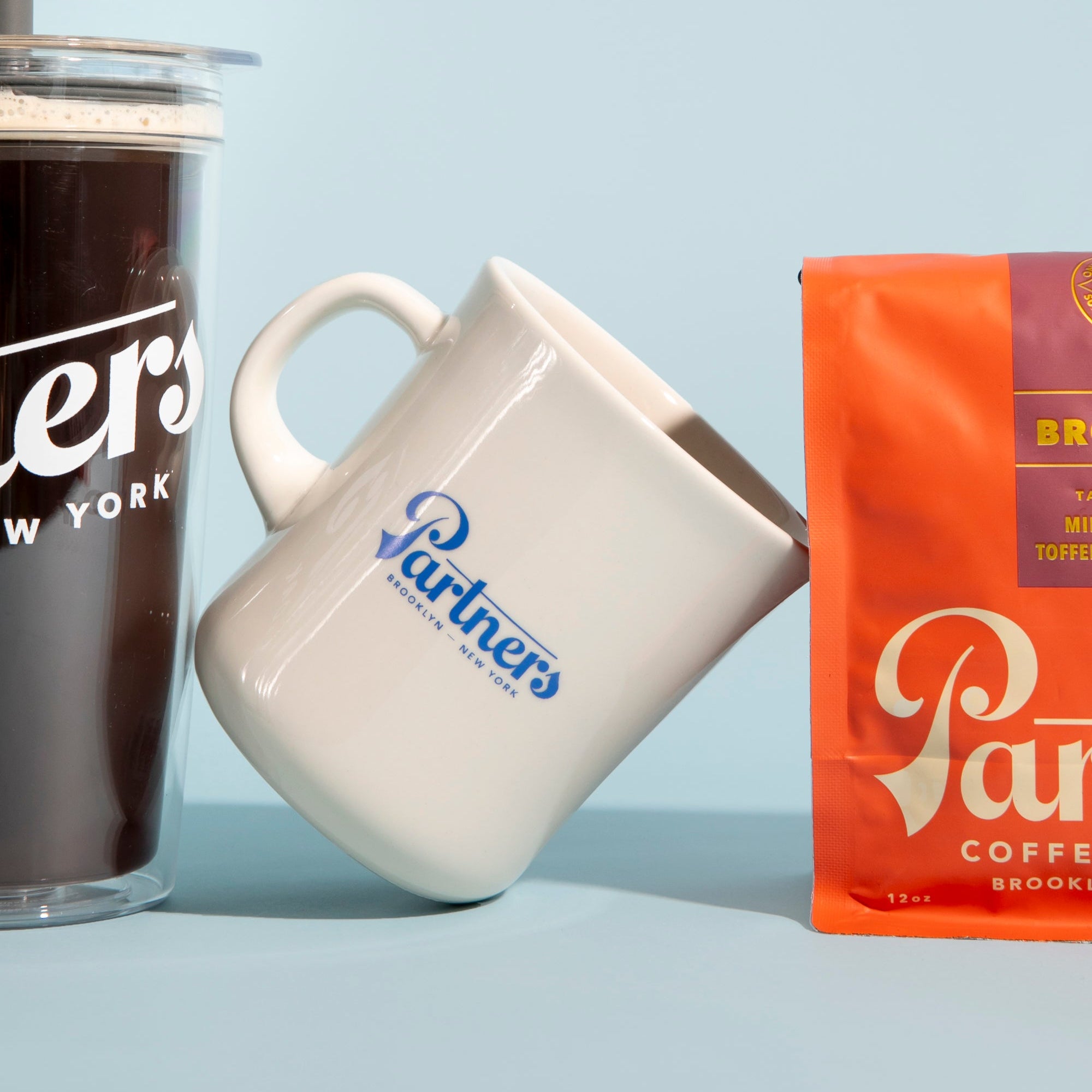 Angled view of Kinto Diner mug showcasing blue Partners logo on white porcelain, 400ml capacity on a light blue background