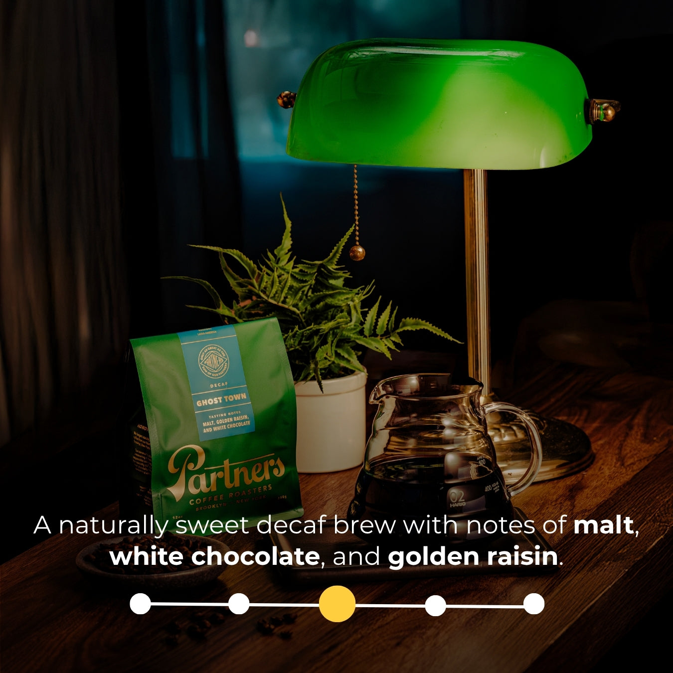 Ghost Town decaf bag beside glass carafe and green lamp on wooden table; overlay: sweet decaf with malt, white choc, and raisin notes