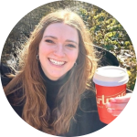 Woman smiling and holding a red takeaway coffee cup in a sunlit outdoor setting
