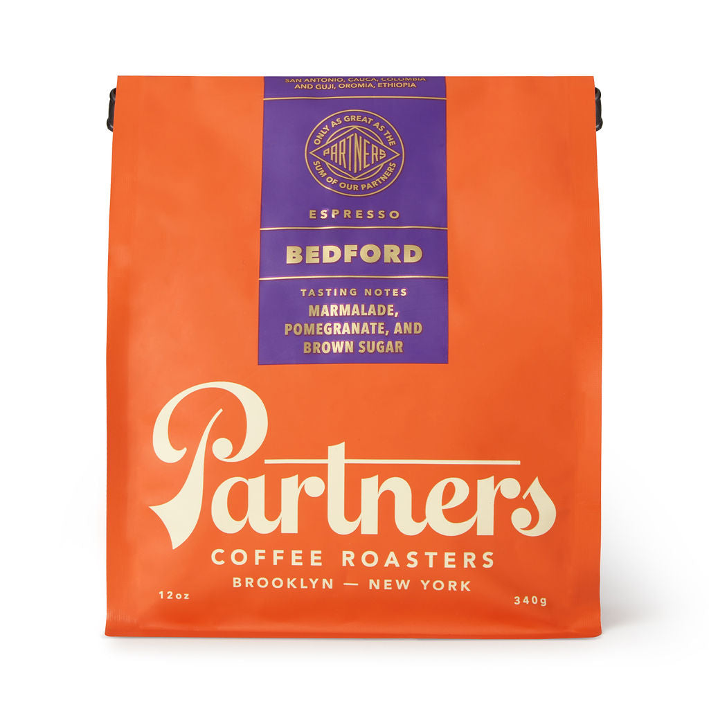 Front view of Bedford coffee bag showing bright orange packaging, purple top label with round logo and white Partners script on white background