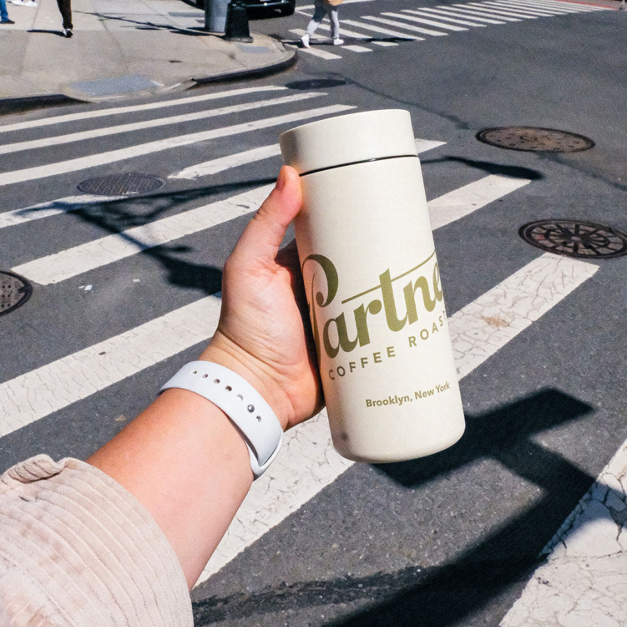 Handheld view of MiiR 360 Traveler in Sandstone showing Partners Coffee logo and closed 360-degree lid over crosswalk