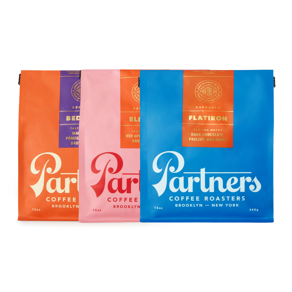 Front view of 3 x 12 oz coffee bags (Flatiron blue, Elevate pink, Bedford orange) on white background