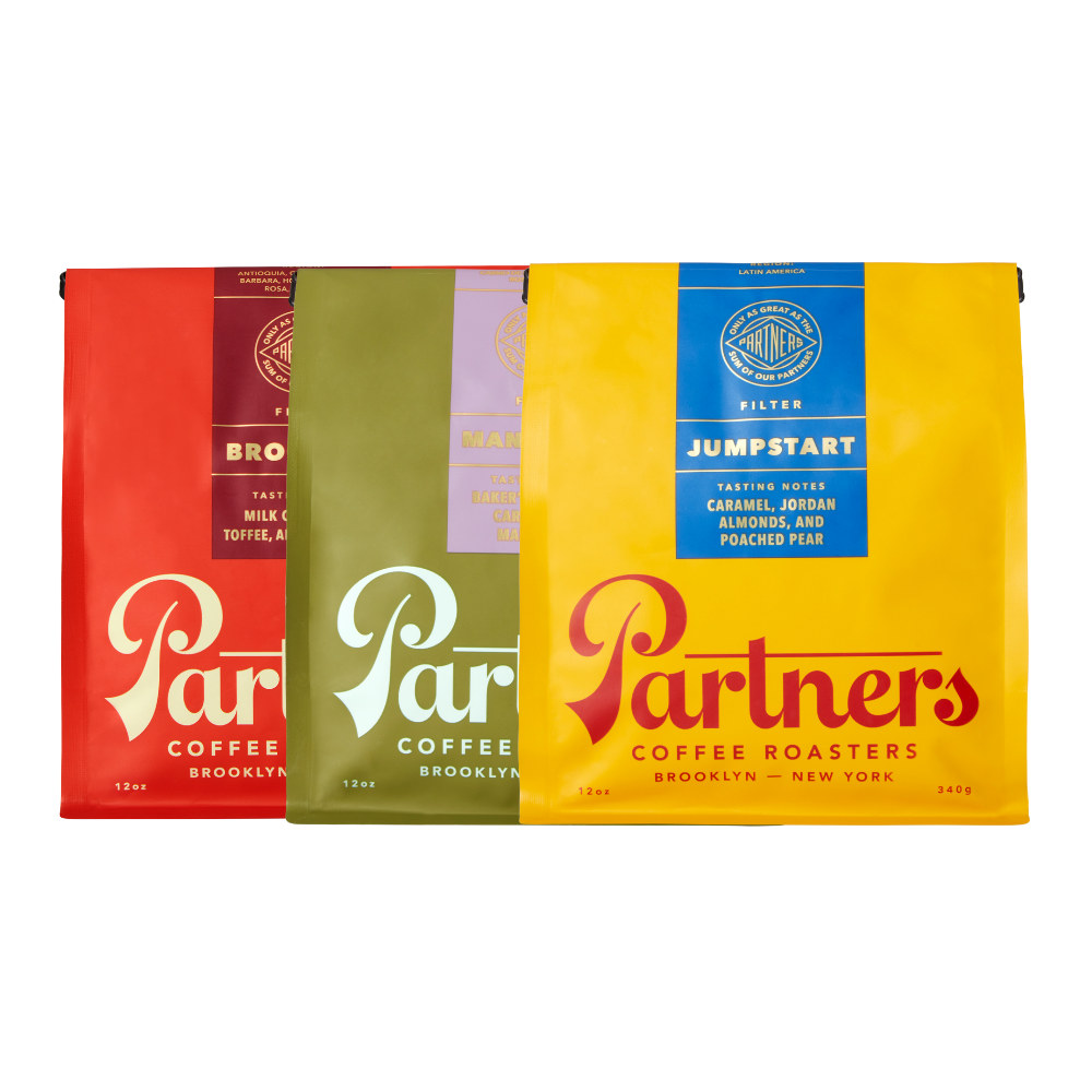 Front view of three 12 oz coffee bags (Jumpstart yellow, Manhattan green, Brooklyn red) packaging on white background